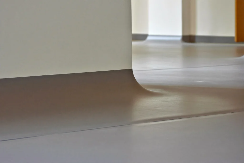 Seamless grey resin floor meeting the wall in a rounded edge in an empty corridor