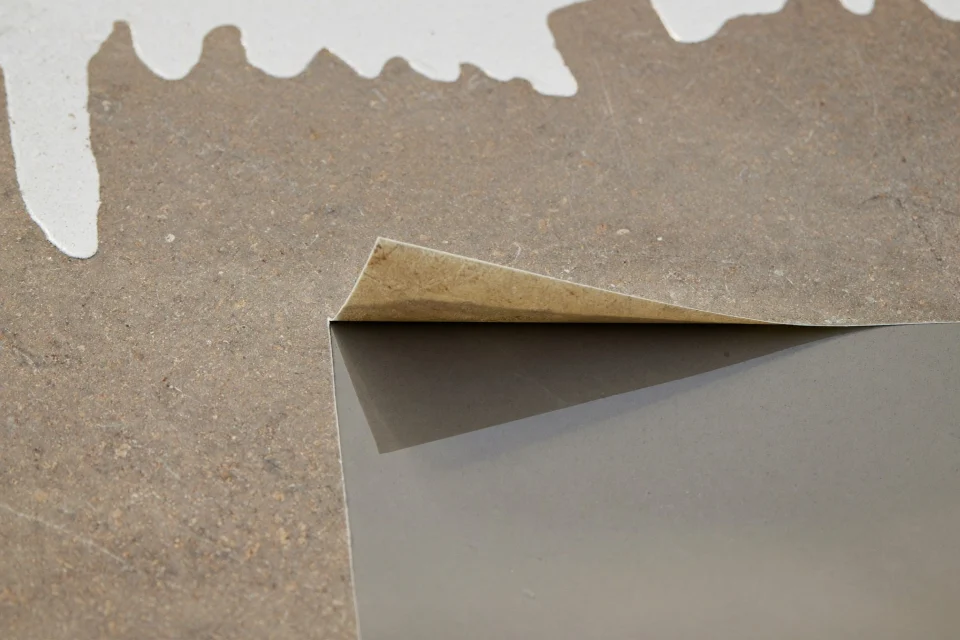 Lifted vinyl sheet revealing damp concrete, resin sample beside it