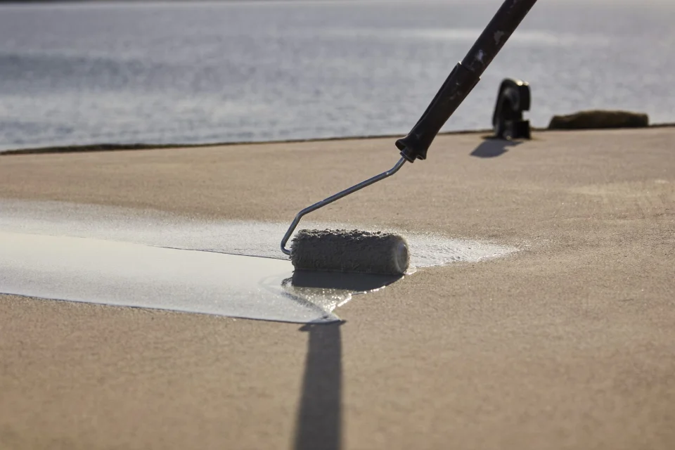 Roller applying a satin coating to an exterior concrete deck by the water